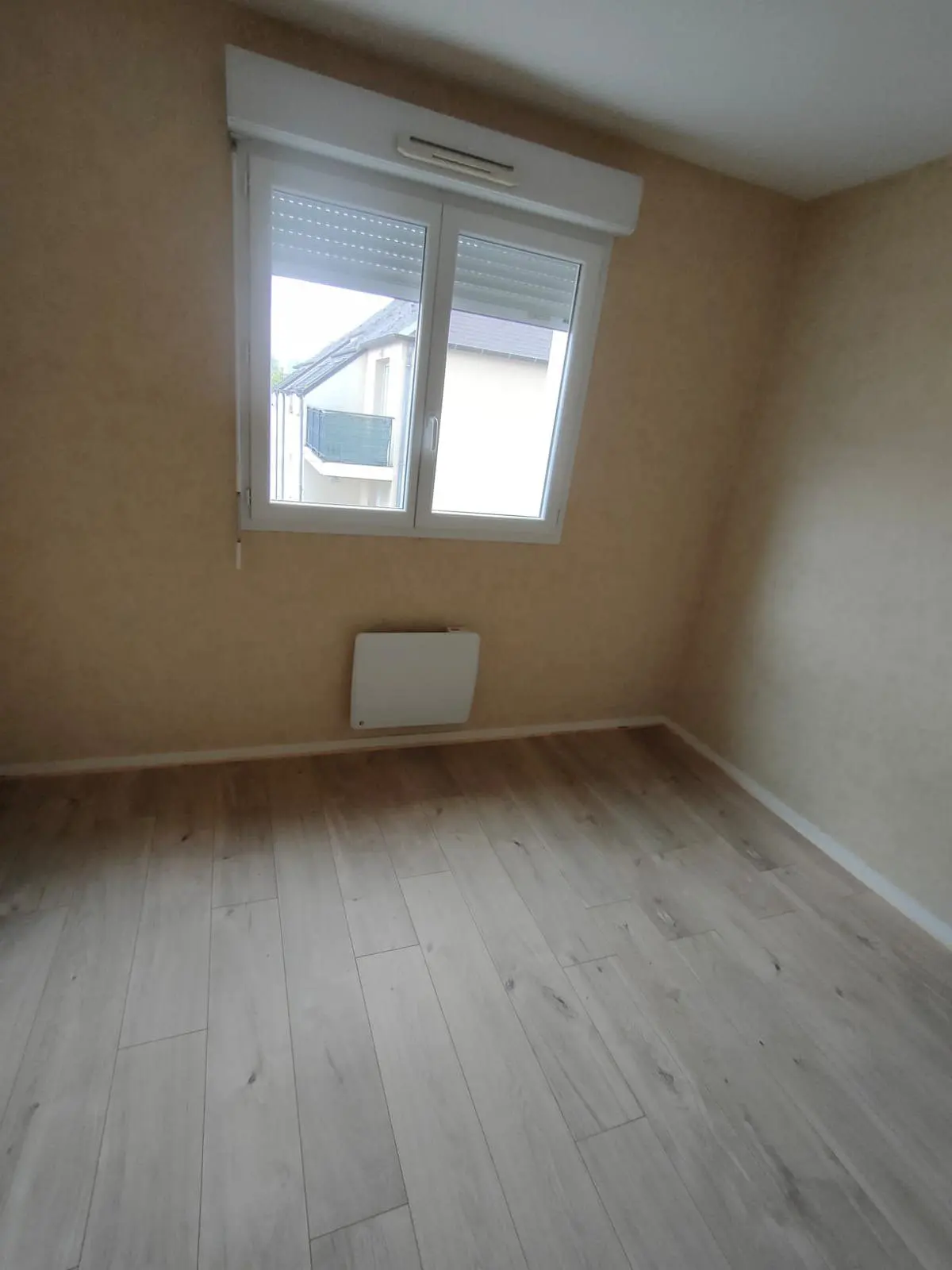 Chambre vide repeinte, parquet stratifié clair et fenêtre plein cadre.