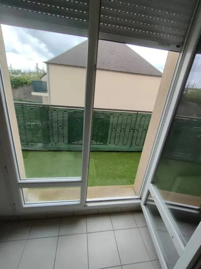 Baie vitrée ouverte sur le balcon et la pelouse en contrebas.