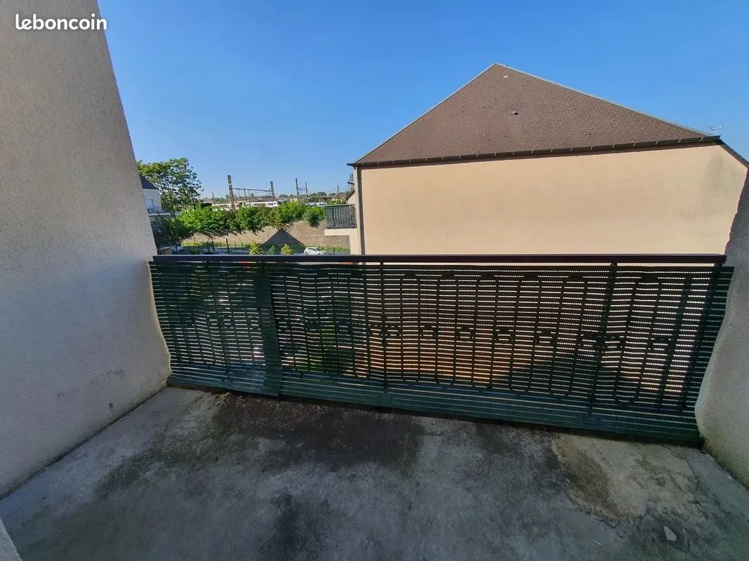 Balcon en béton avec garde-corps métallique, vue sur les toits.