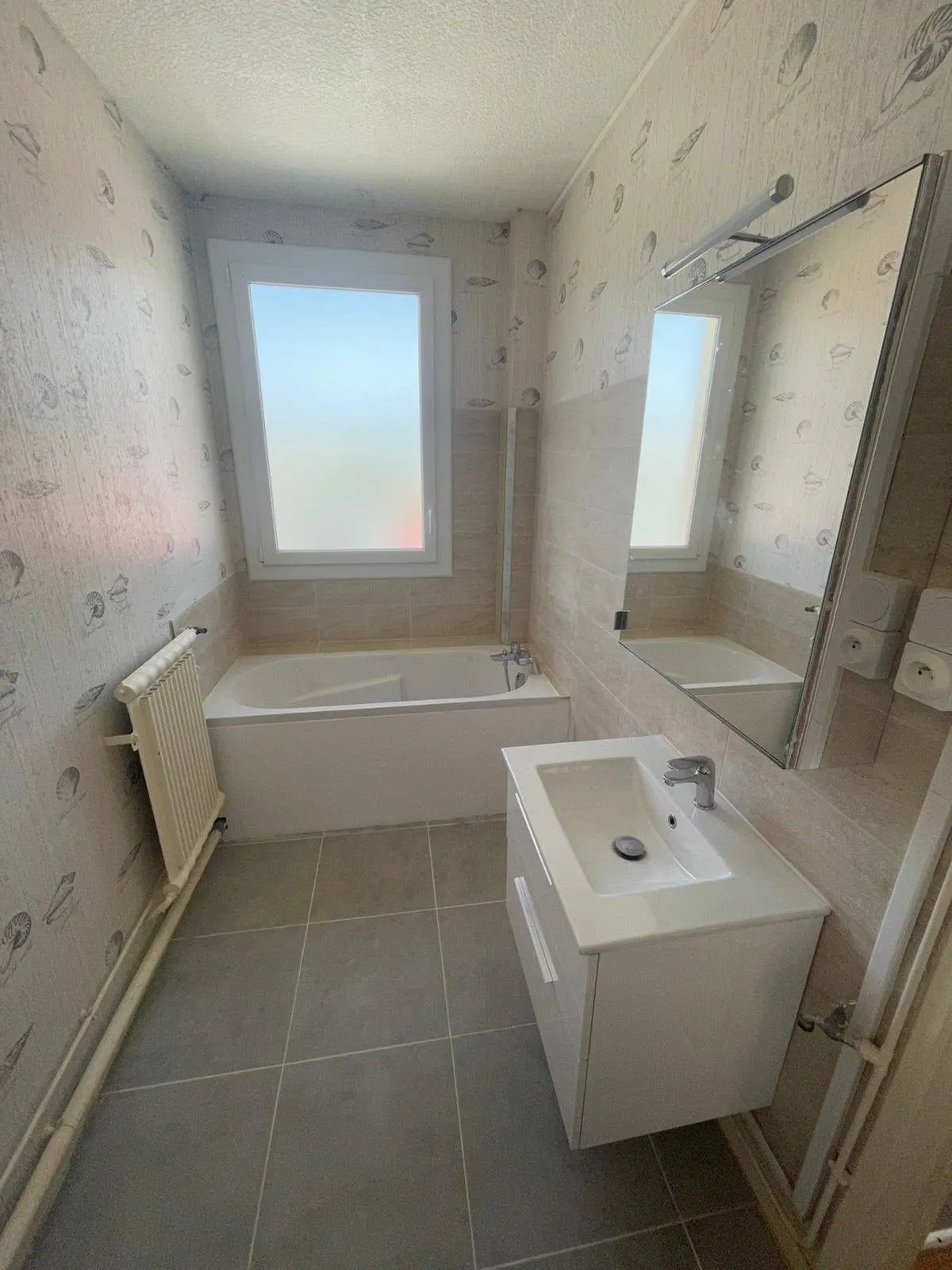 Salle de bains refaite : baignoire, meuble vasque suspendu et grand miroir.