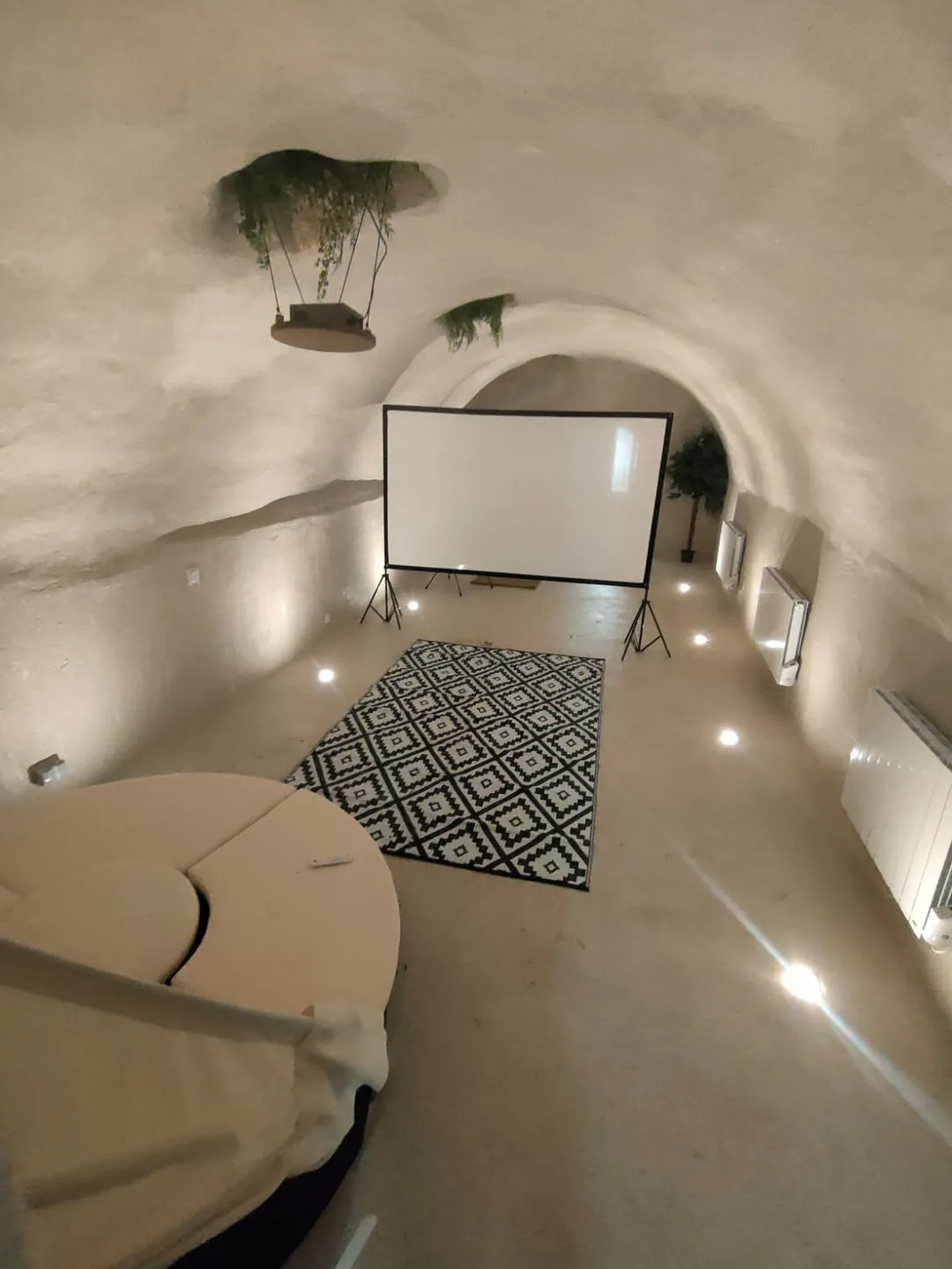 La cave voûtée après travaux : murs et voûte enduits en blanc, écran de projection, tapis graphique, spots encastrés.