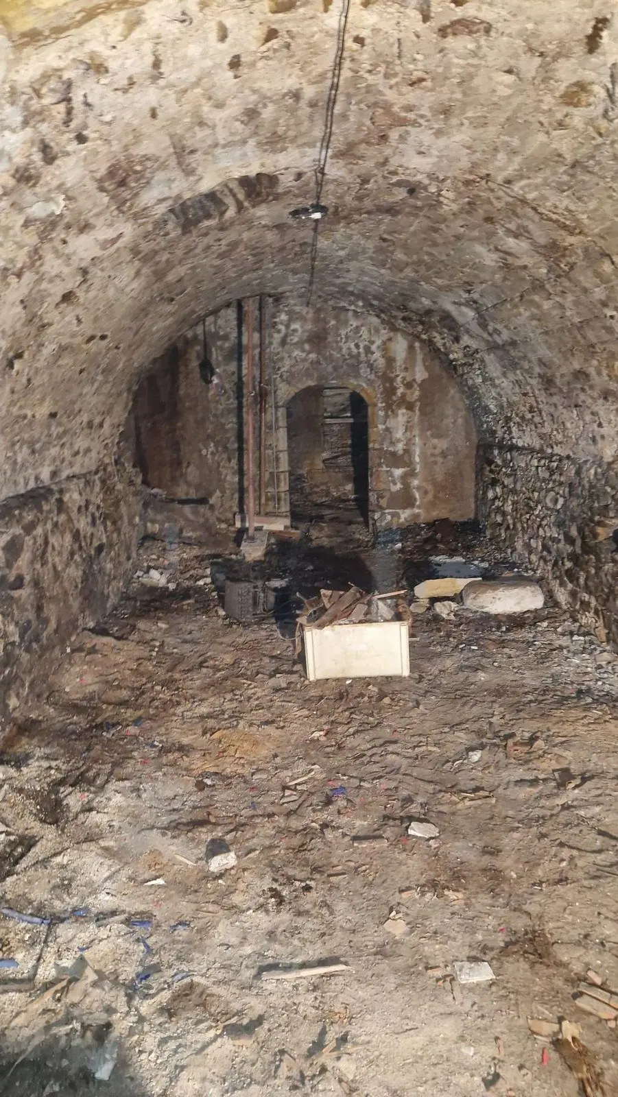 Cave voûtée en pierre avant travaux, sol en terre battue jonché de gravats.