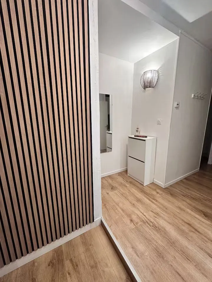 Couloir habillé d'un mur de tasseaux bois, applique murale et parquet clair.