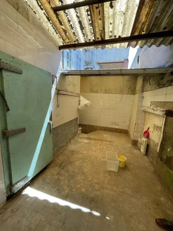 Cour bétonnée avant travaux, porte de garage verte, couverture en tôle ondulée.