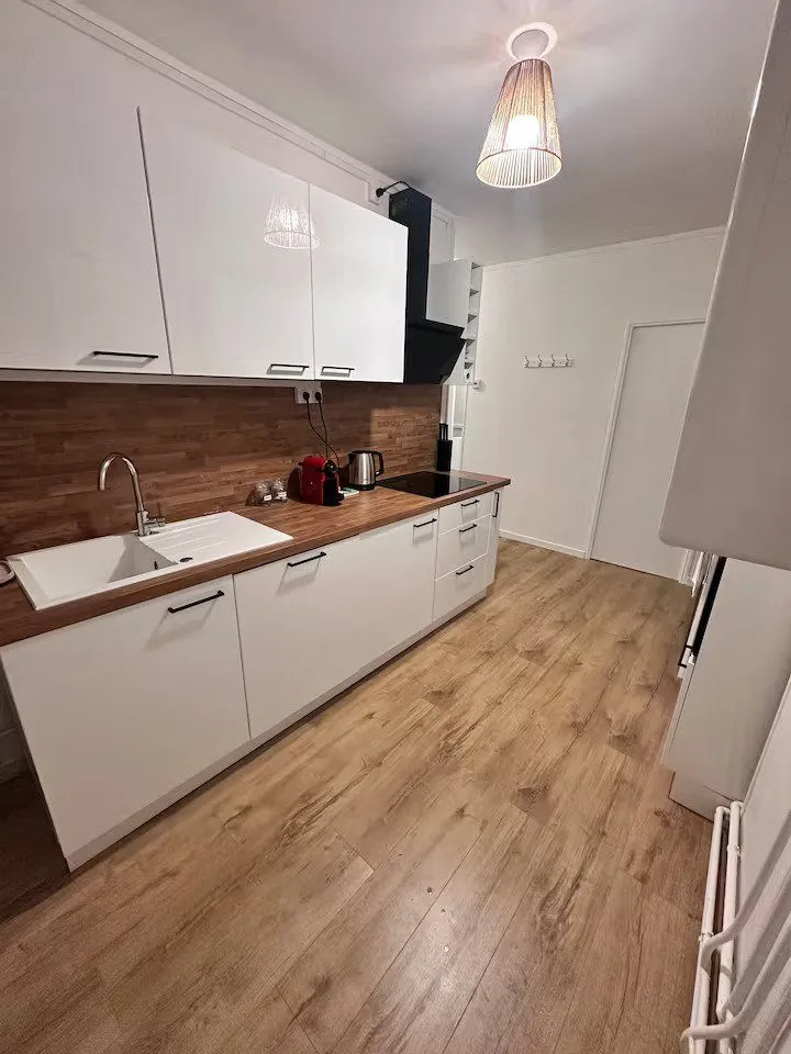 Cuisine neuve : façades blanches, plan de travail bois et évier sous la fenêtre.
