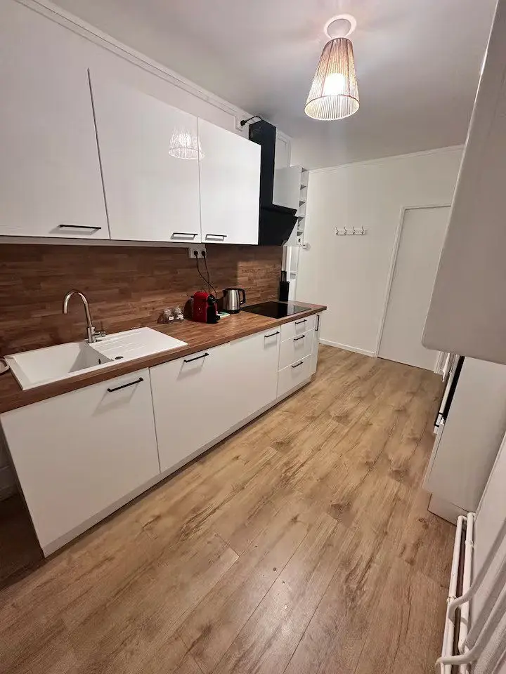La même cuisine après travaux : façades blanches, plan de travail bois et évier sous la fenêtre.
