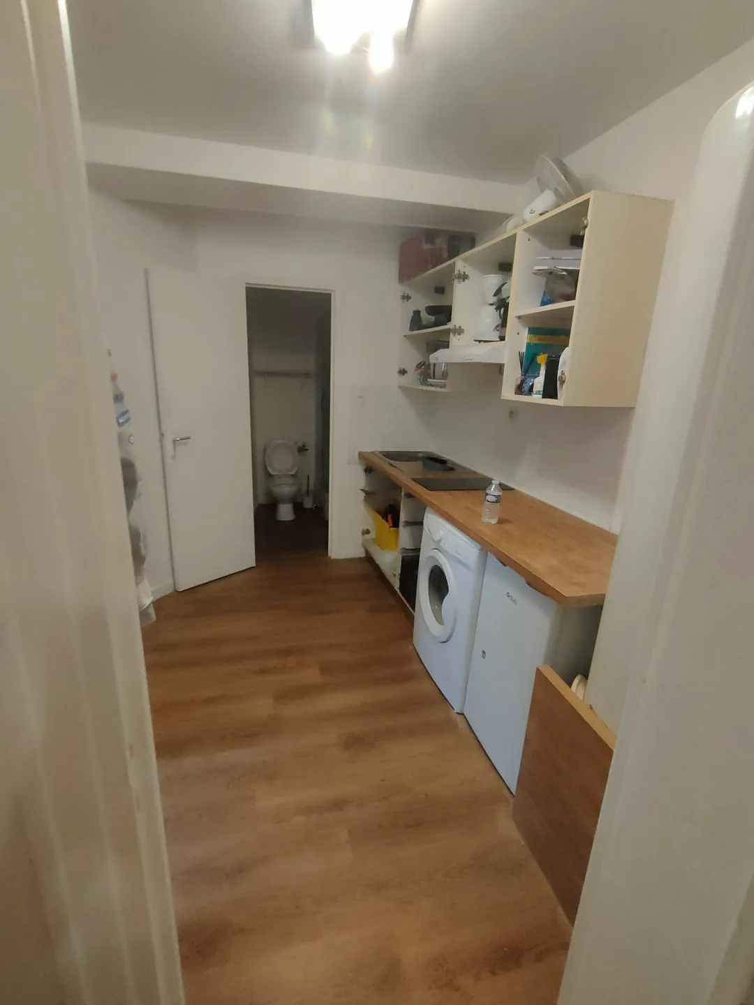 Cuisine refaite vue depuis le séjour : plan de travail bois, lave-linge intégré, étagères hautes.