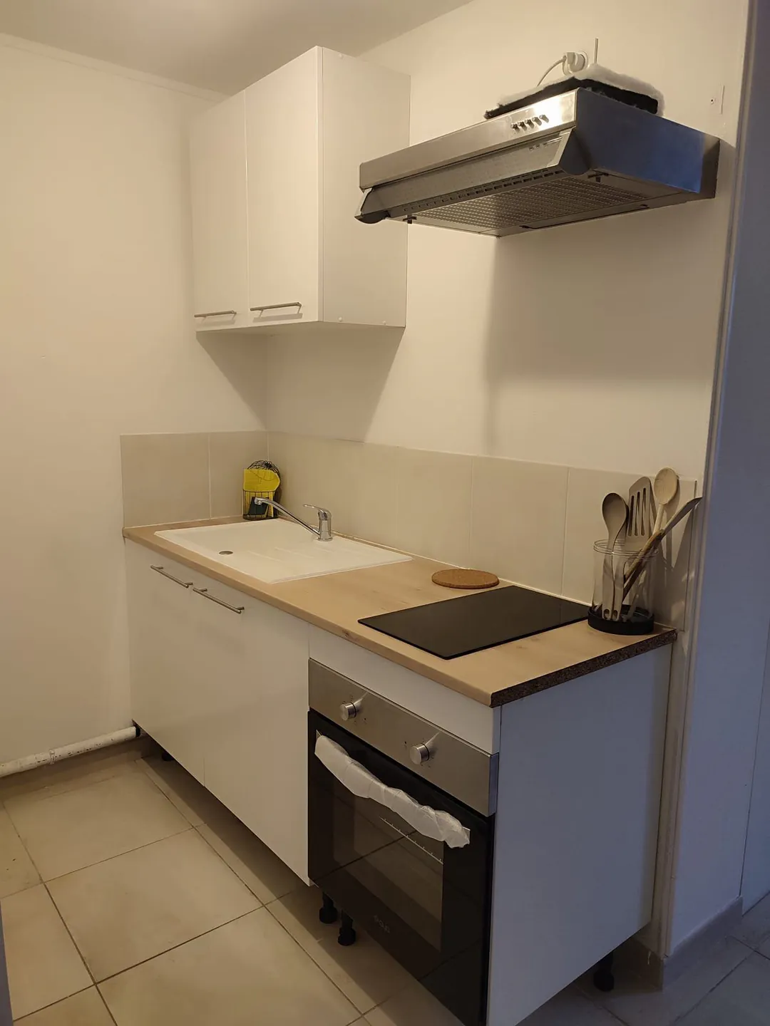 Kitchenette neuve : hotte, plaque de cuisson, four et plan de travail bois.