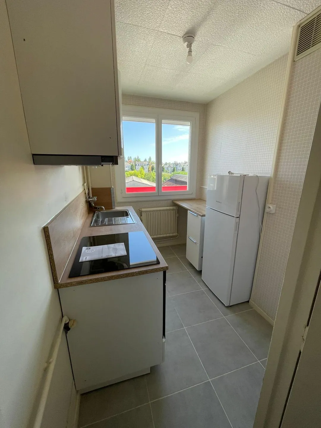 Cuisine équipée avec plaque, hotte, réfrigérateur et sol carrelé.