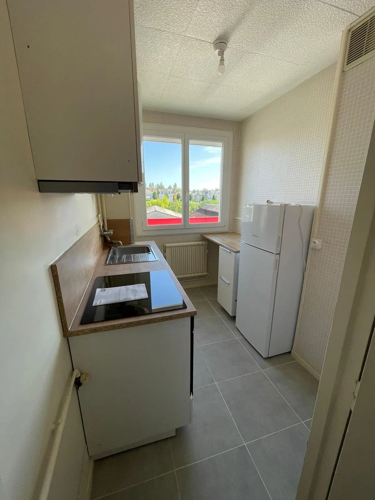 Cuisine équipée avec plaque, hotte, réfrigérateur et sol carrelé.