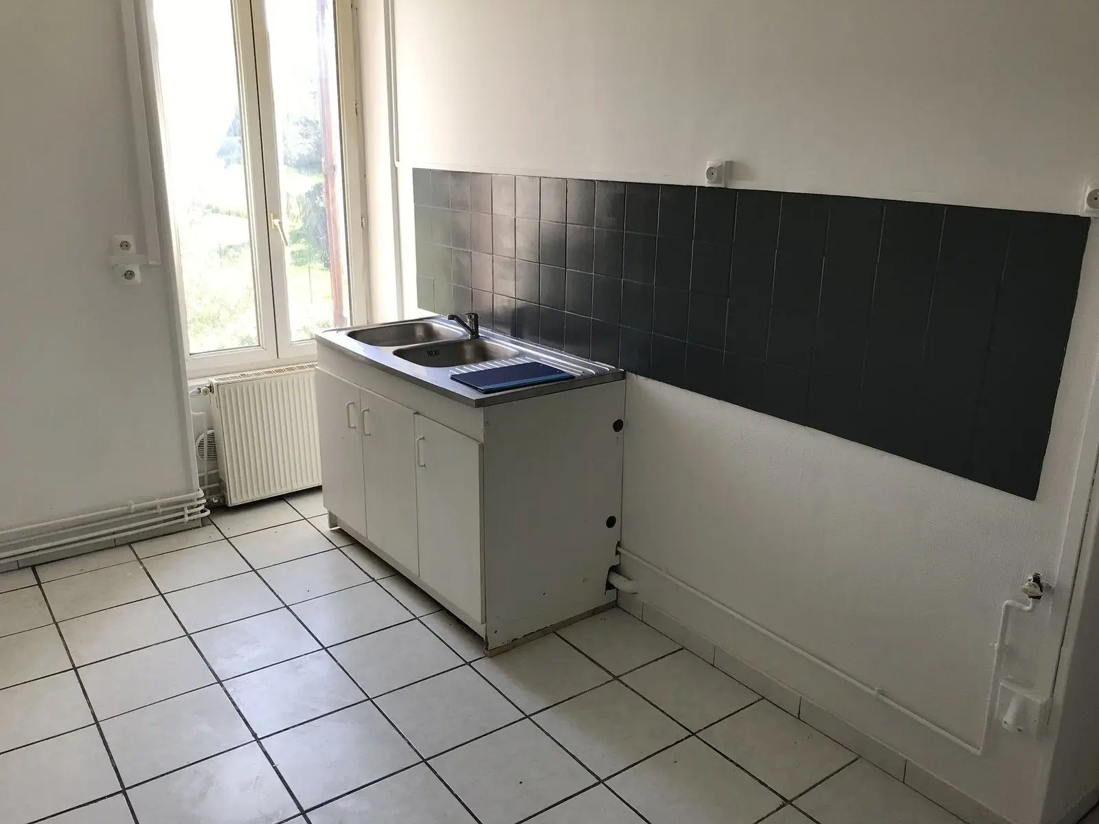 La cuisine d'origine : plan de travail carrelé le long du mur, sol en carrelage clair.