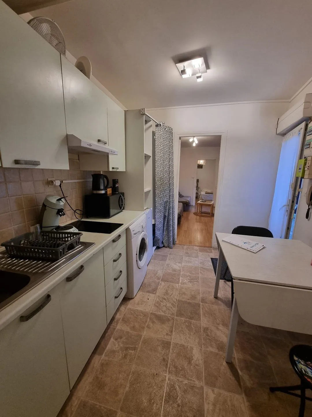 Vue en enfilade depuis la cuisine, sol carrelé sombre, vers le fond du logement.