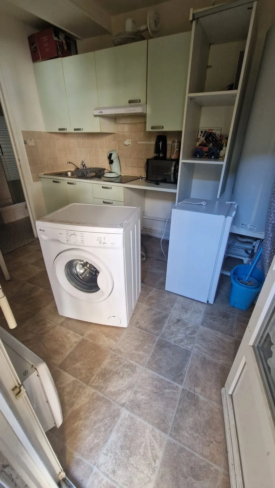 Cuisine en cours de vidage : lave-linge et réfrigérateur déplacés sur l'ancien carrelage.