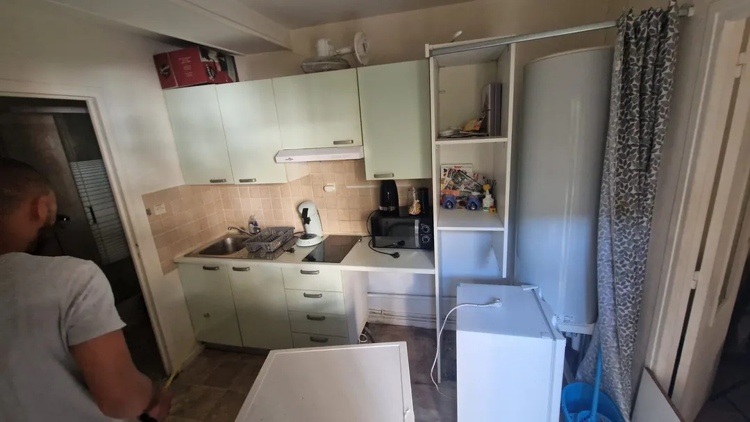 Un artisan au travail devant la cuisine démontée, réfrigérateur écarté du mur.