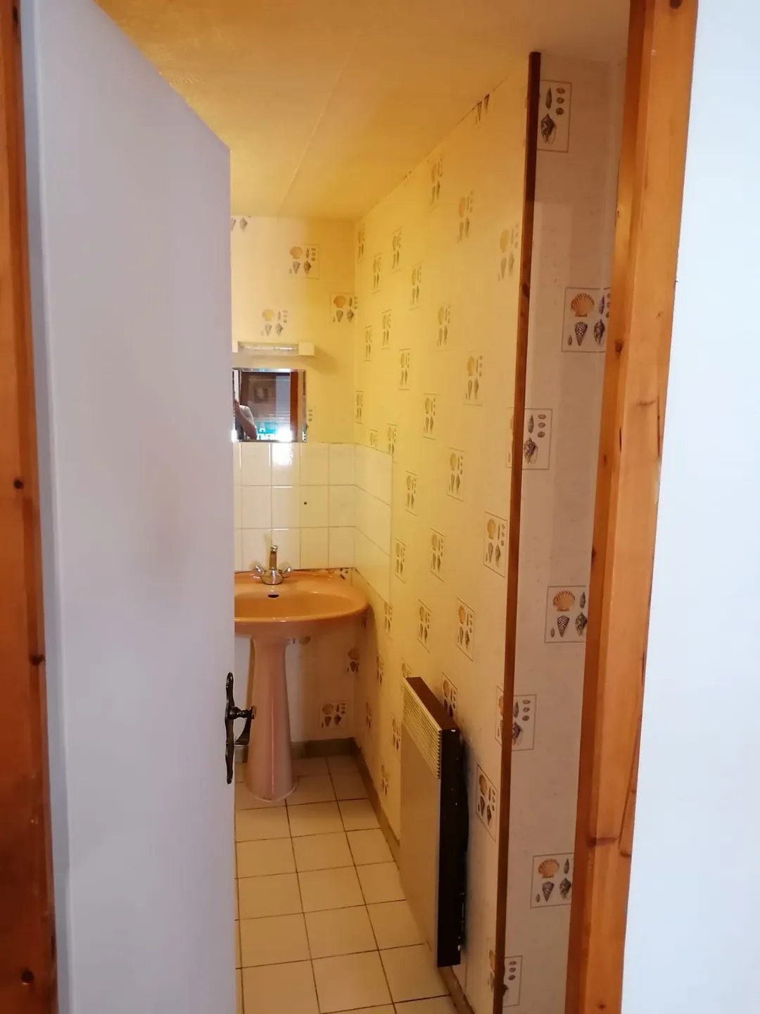 Lavabo d'origine dans un renfoncement tapissé de papier peint à motifs.