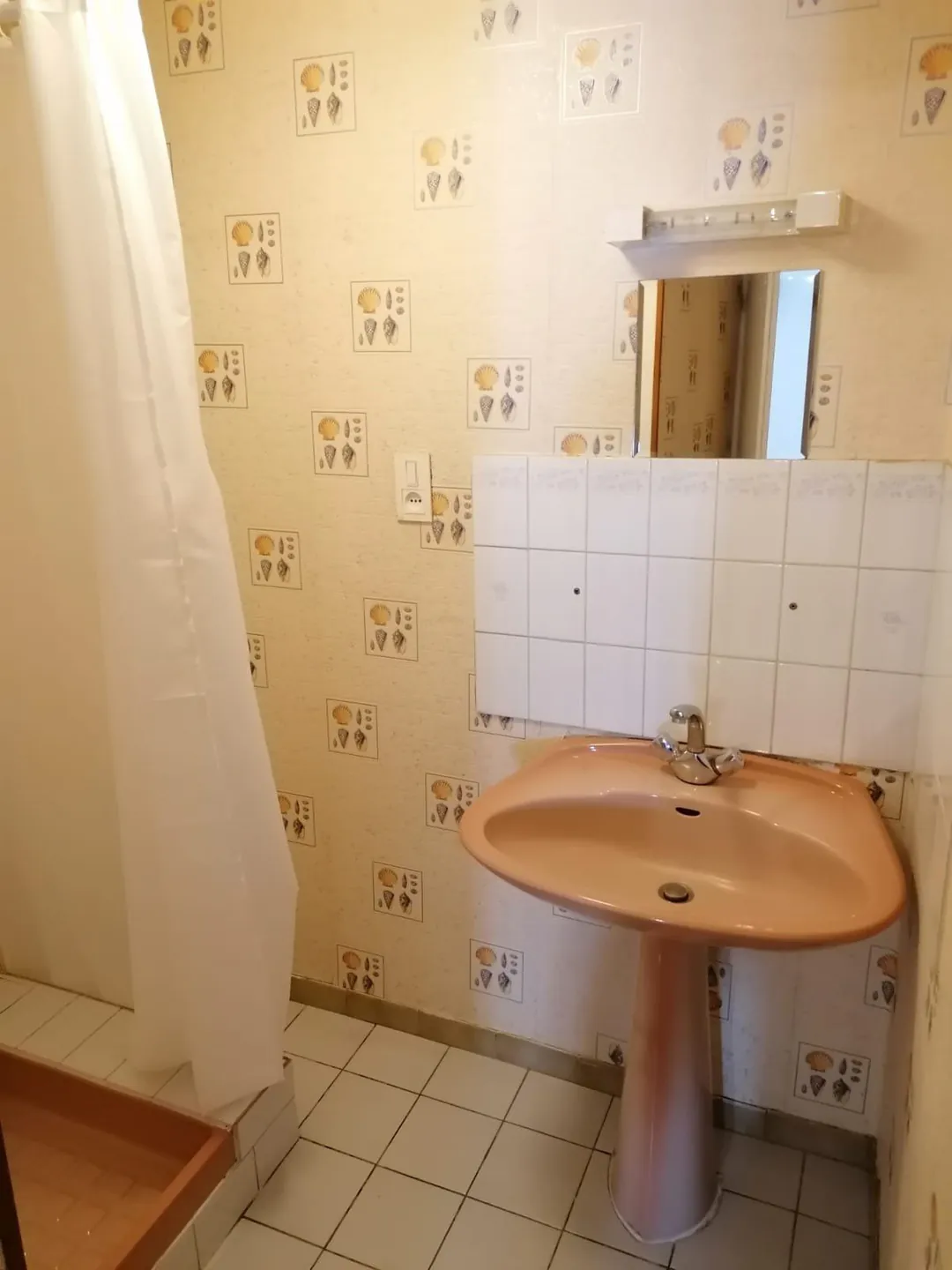 Salle d'eau d'origine : lavabo saumon sur colonne, miroir et papier peint à motifs.