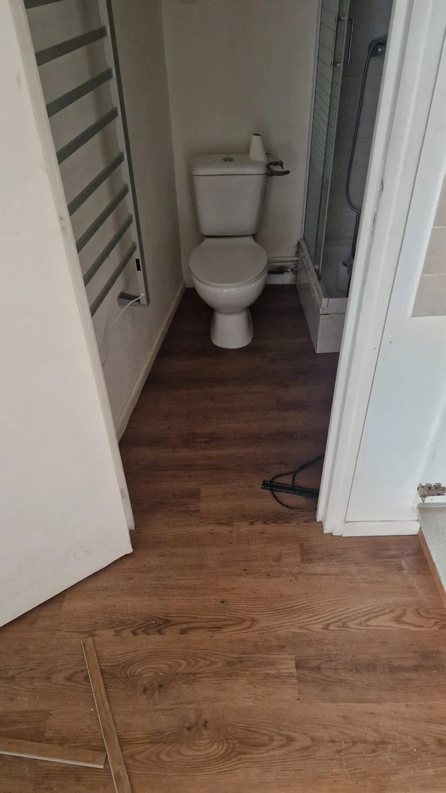 Le couloir vers la salle d'eau, sol neuf posé, porte du WC ouverte.