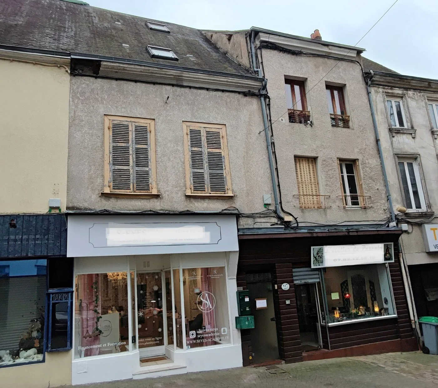 Façade de l'immeuble de rapport : deux vitrines commerciales en rez-de-chaussée, deux niveaux d'habitation au-dessus.