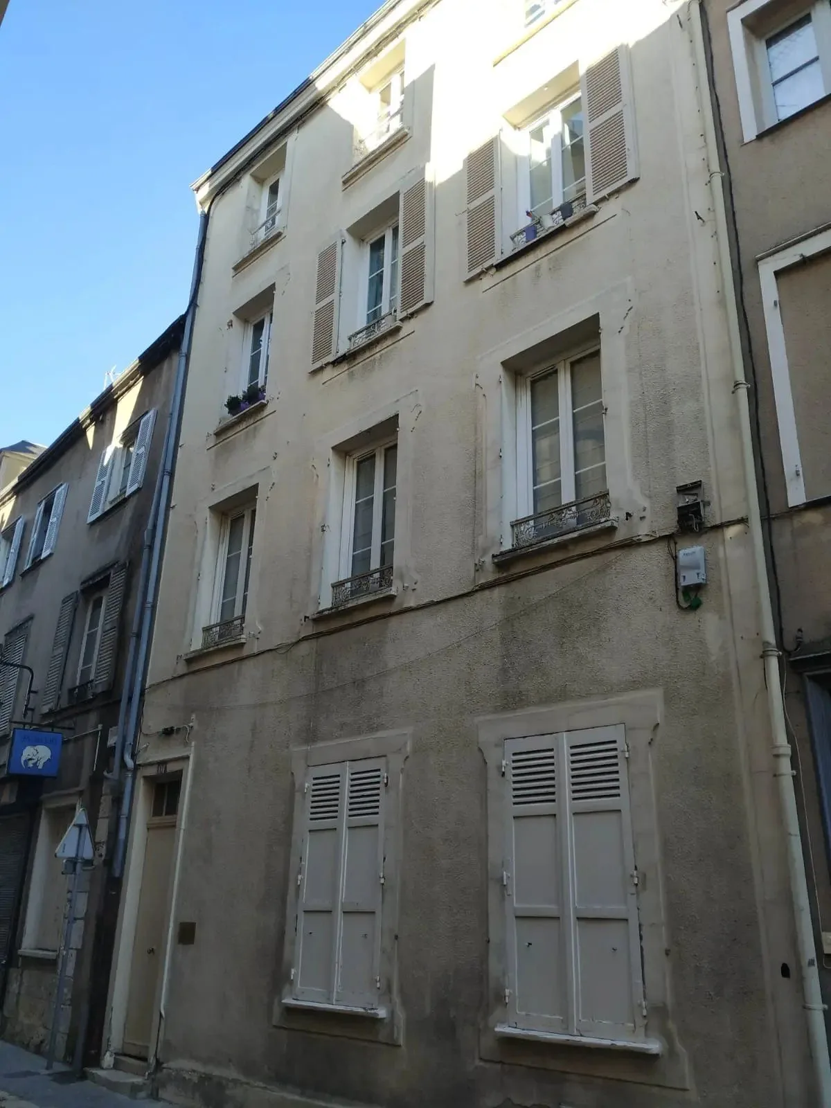 Rue ancienne bordée d'immeubles en pierre aux volets clairs.