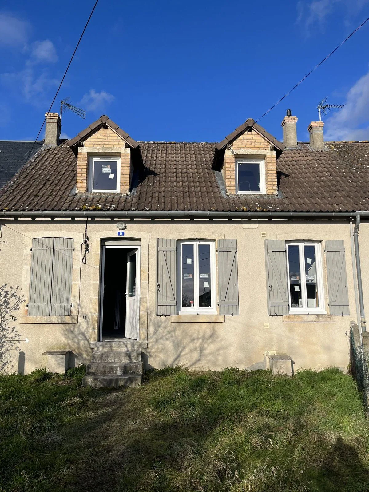 Deux maisons mitoyennes en pierre avec lucarnes et volets, devant une pelouse.
