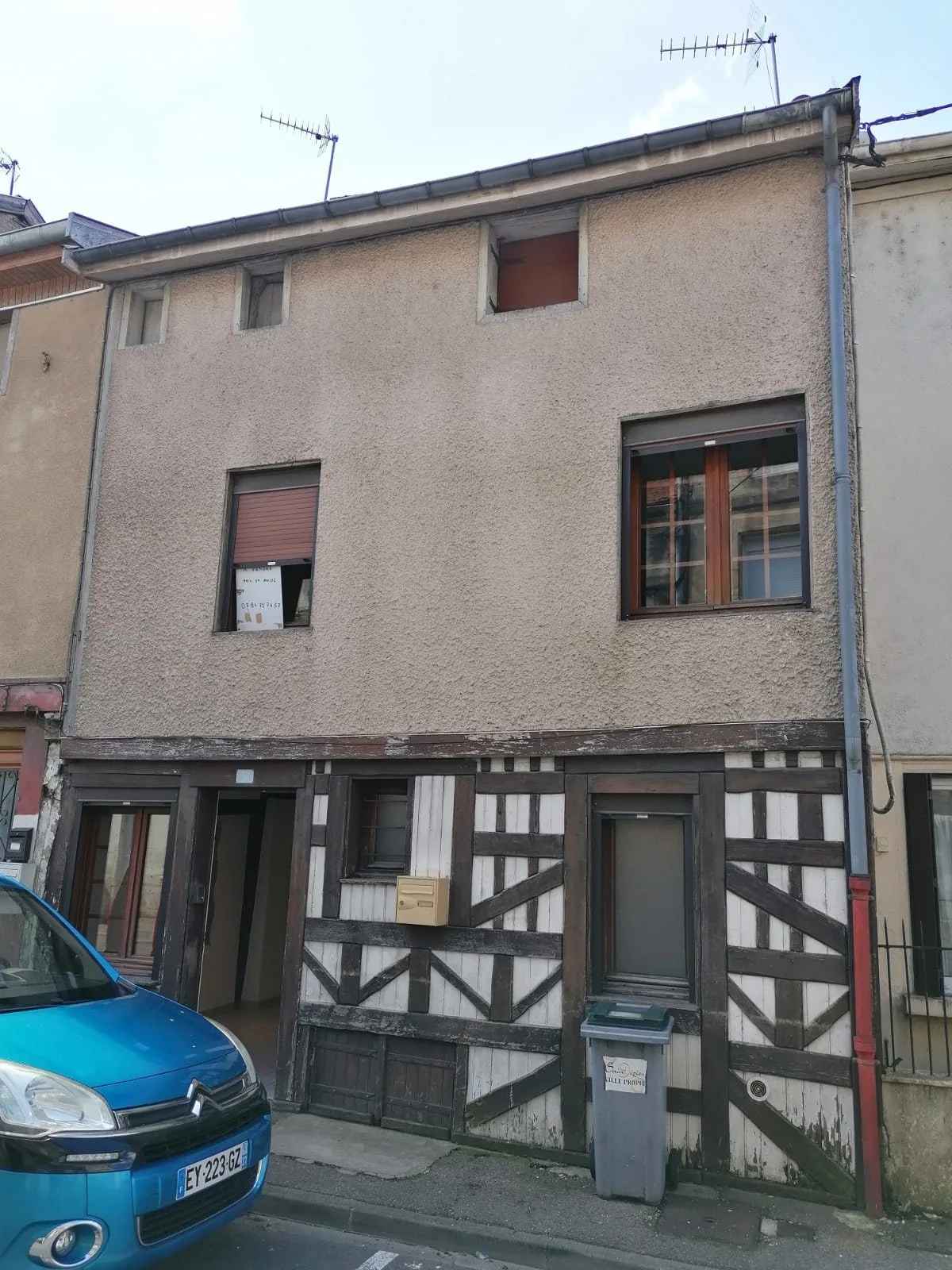 Maison de ville à colombages, façade sur rue, volets bois et voiture bleue devant.