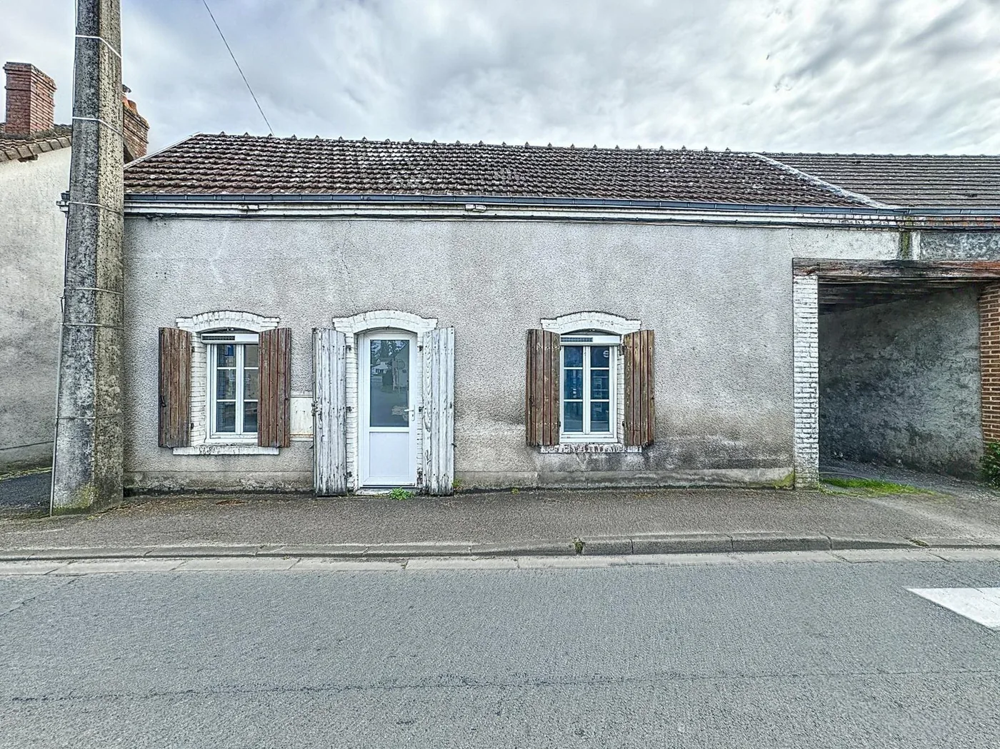 Maison de plain-pied en pierre enduite, façade sur rue, volets clairs.