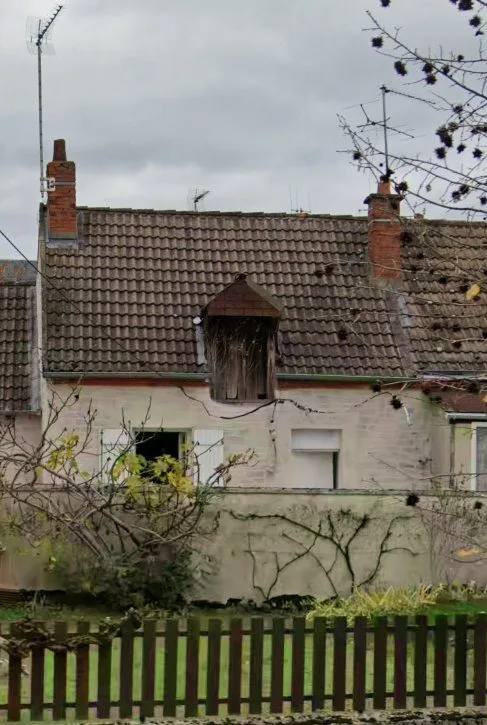 Maison de village ancienne, façade enduite, lucarne à toit pointu et volets bois.