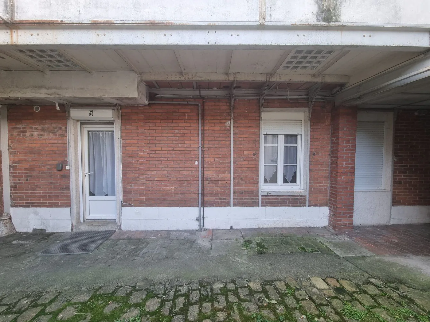 Bâtiment en brique rouge avec une cour pavée à l'avant.