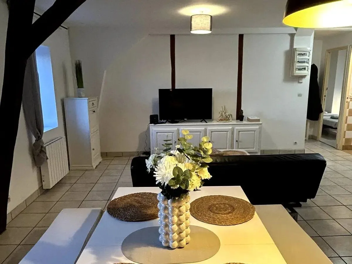 Pièce de vie meublée sous poutres : table de repas, canapé et télévision.