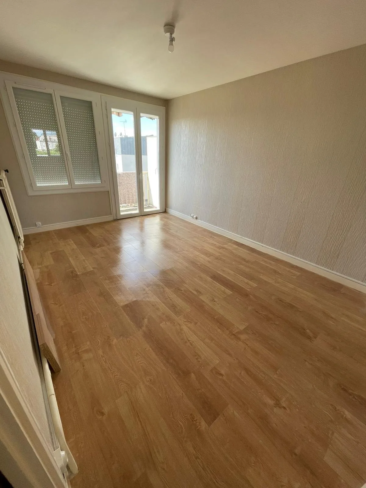 Séjour repris : parquet clair, murs blancs et grande fenêtre.