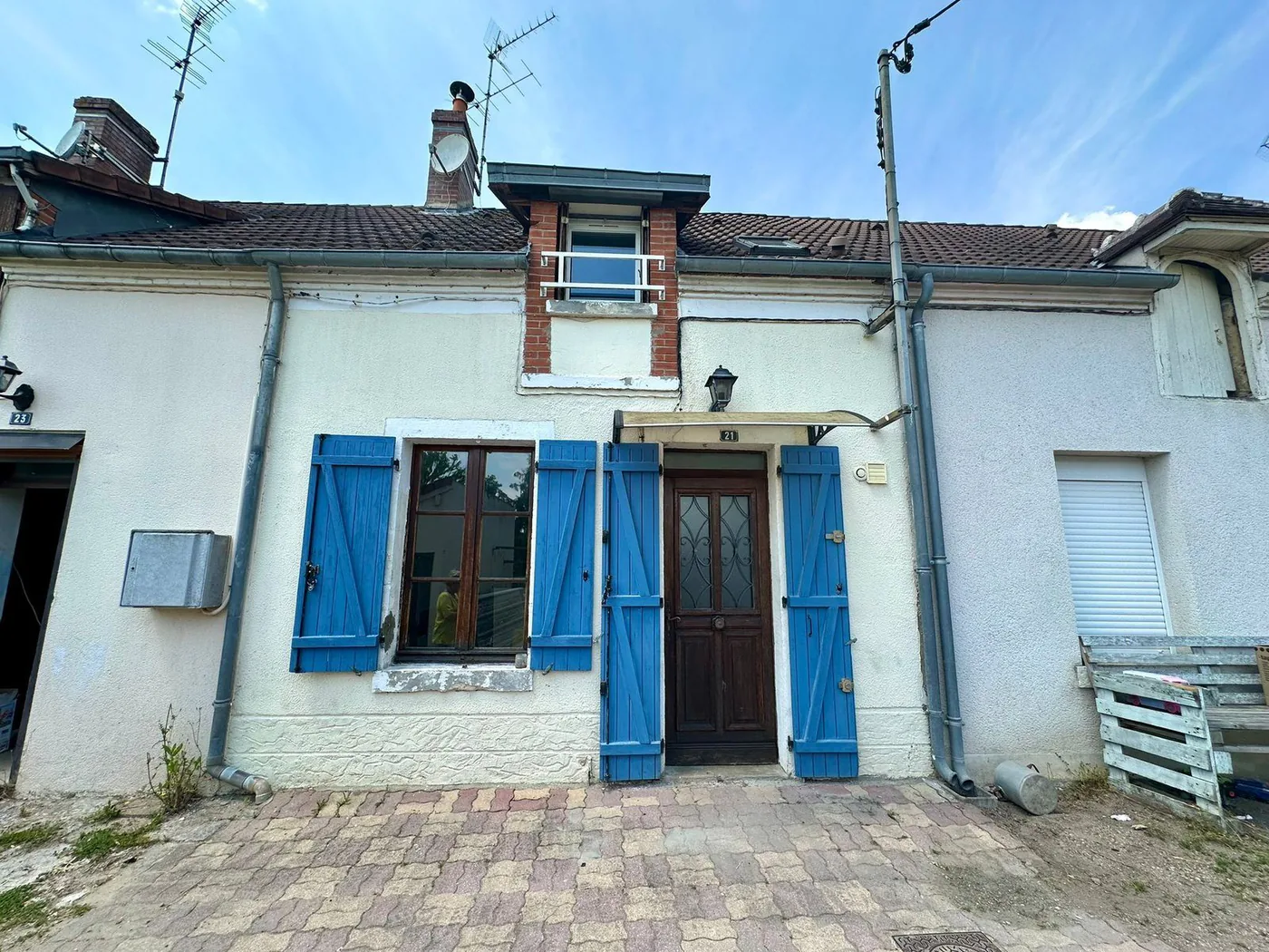 Maison de village mitoyenne, façade blanche et volets bleus, cour pavée devant.