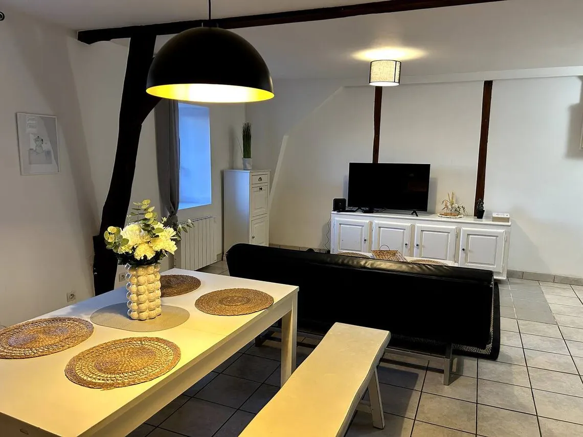 Table de repas en bois clair sous une suspension noire, bahut au fond.