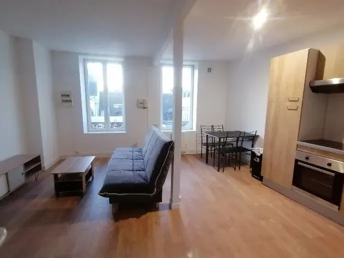 Pièce de vie meublée : canapé, table de repas et cuisine intégrée au fond.