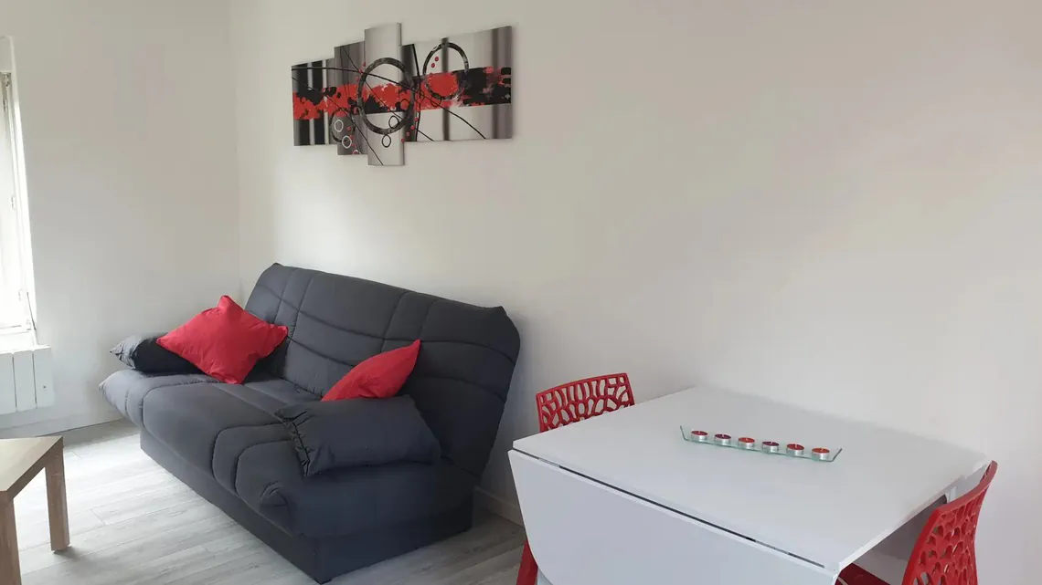 Coin salon avec canapé gris, coussins rouges et table blanche.