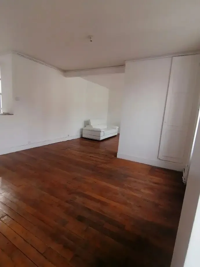 Pièce au parquet ancien avec placard blanc et grande fenêtre.