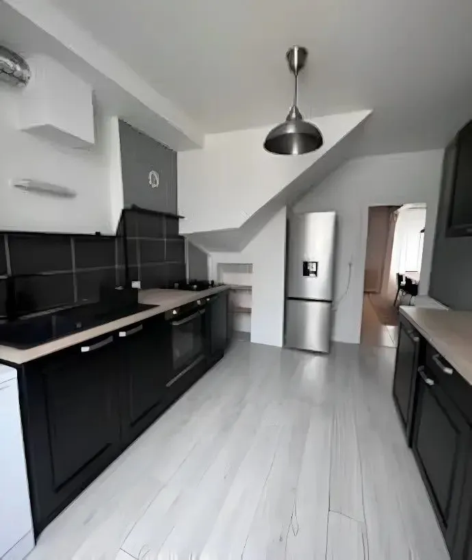 Cuisine noire avec plan de travail bois, réfrigérateur et sol clair.