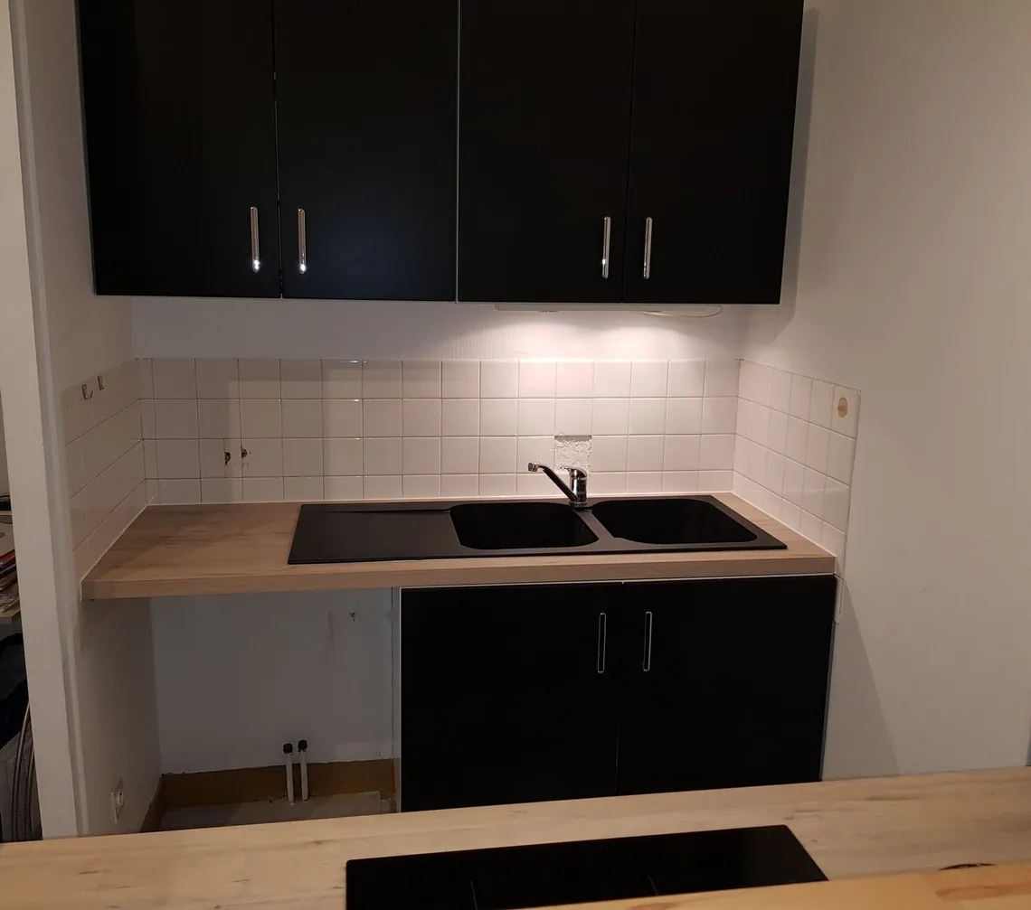 Cuisine linéaire noire et bois avec évier et plaque de cuisson.