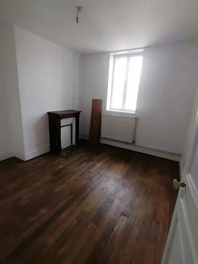 Chambre au parquet ancien, cheminée condamnée et radiateur sous la fenêtre.