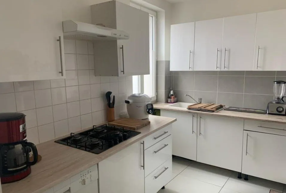 Cuisine équipée blanche avec plaque gaz, hotte et plan de travail bois.