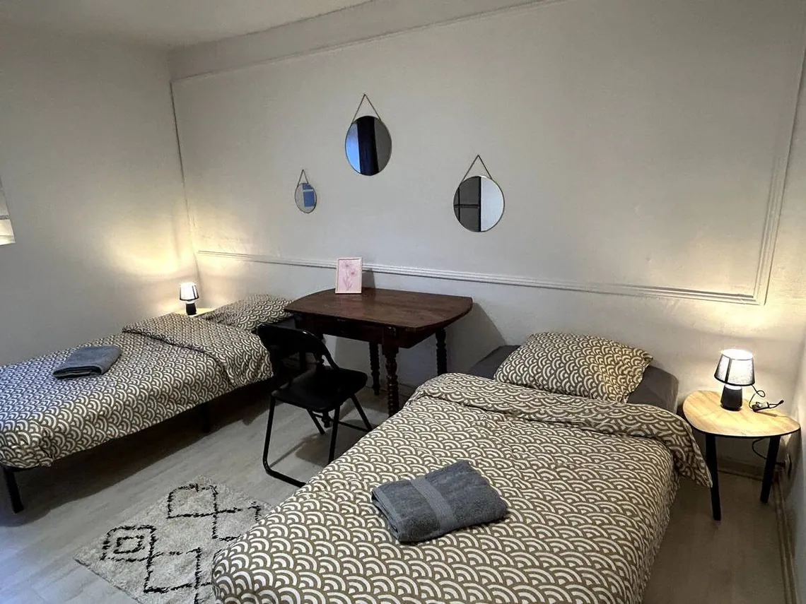 Chambre avec deux lits simples, guéridon et lampe de chevet.