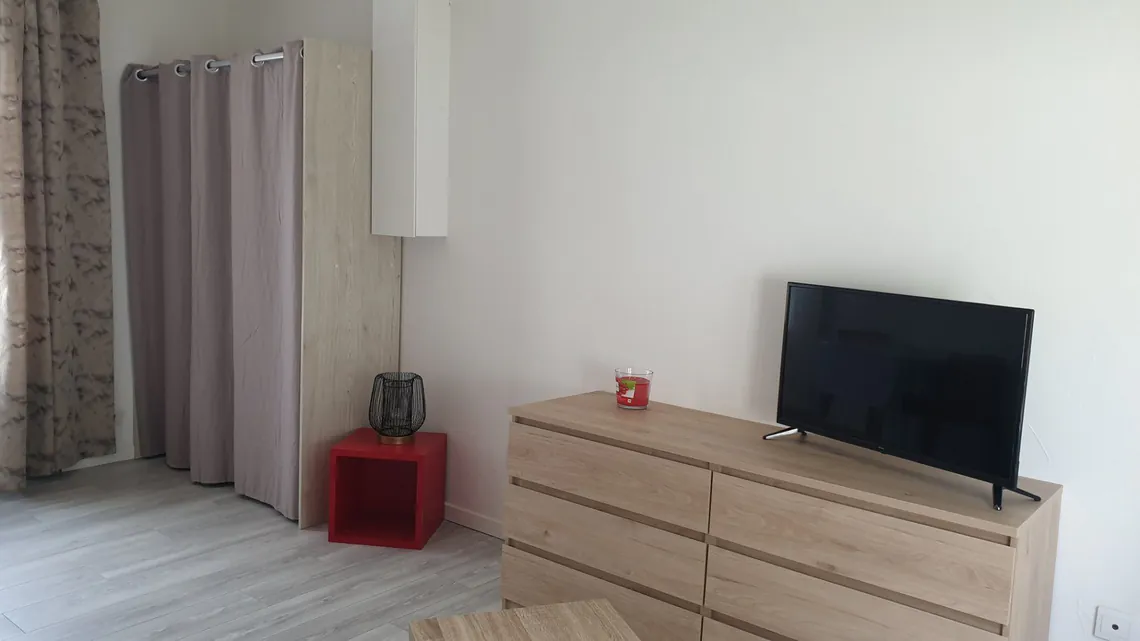 Coin télévision avec commode en bois et rideau de séparation.