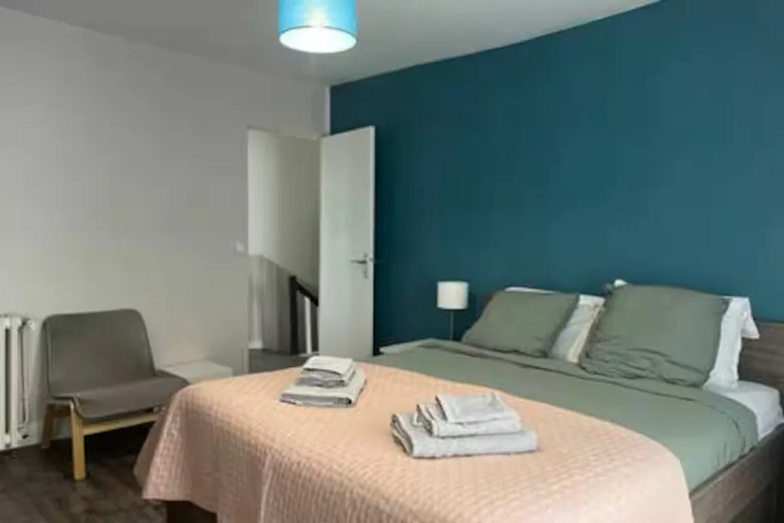 Chambre avec lit double, mur vert d'eau et fauteuil.