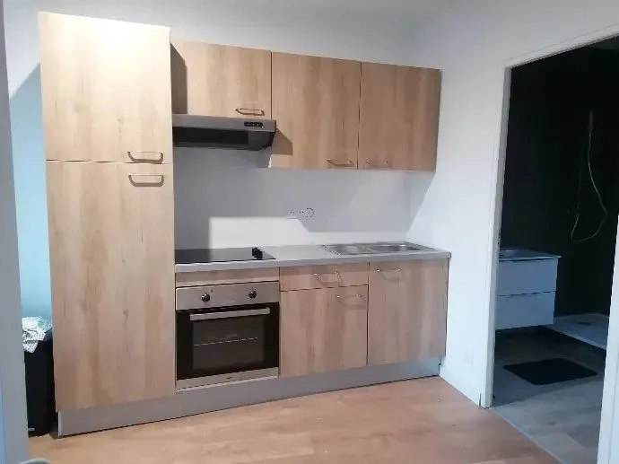 Cuisine équipée bois clair avec four encastré, plaque et évier.