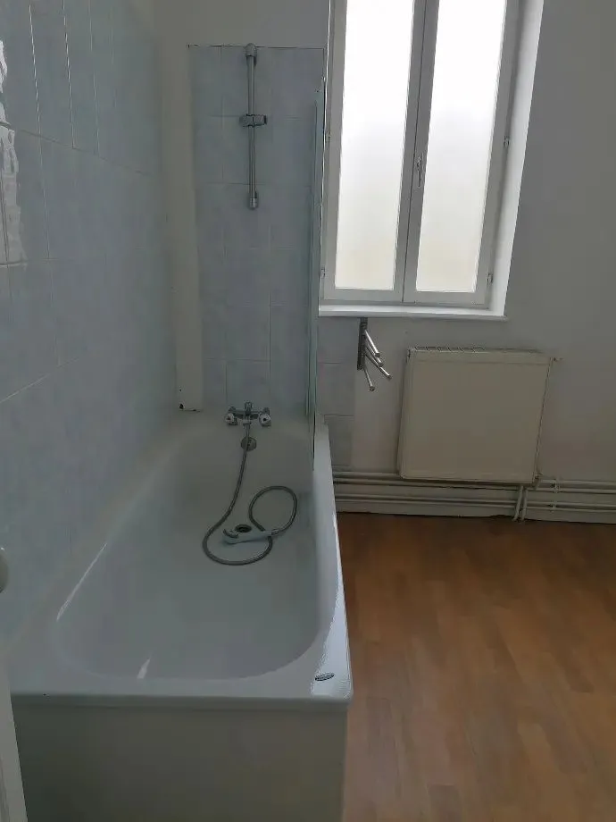 Salle de bains avec baignoire, carrelage bleu clair et fenêtre.