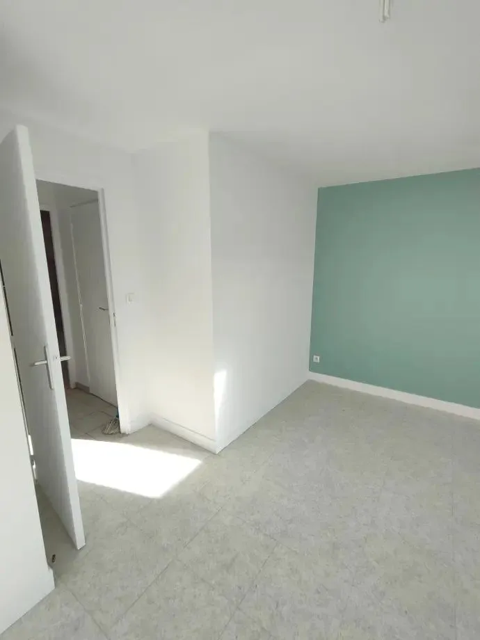 Chambre claire avec mur vert d'eau, moquette et porte ouverte.