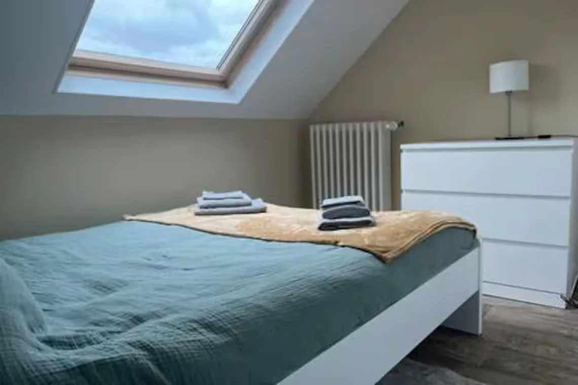 Chambre sous fenêtre de toit avec lit double et commode.