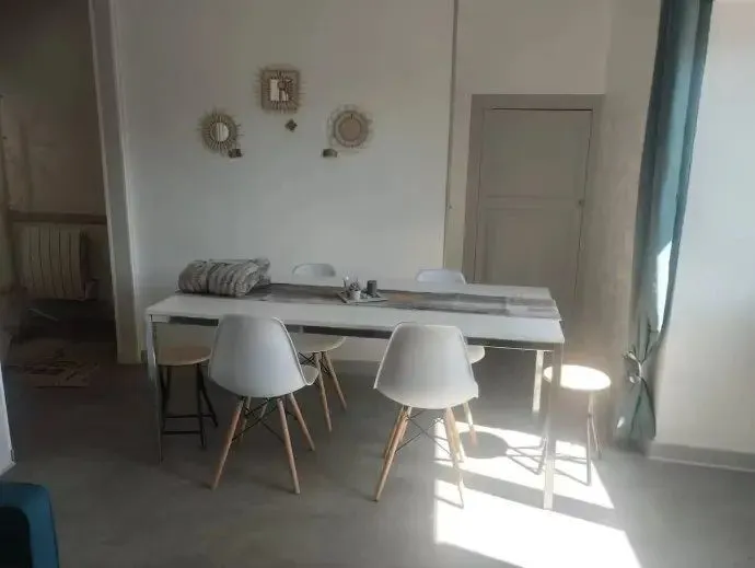 Coin repas avec table blanche, chaises et fenêtres.