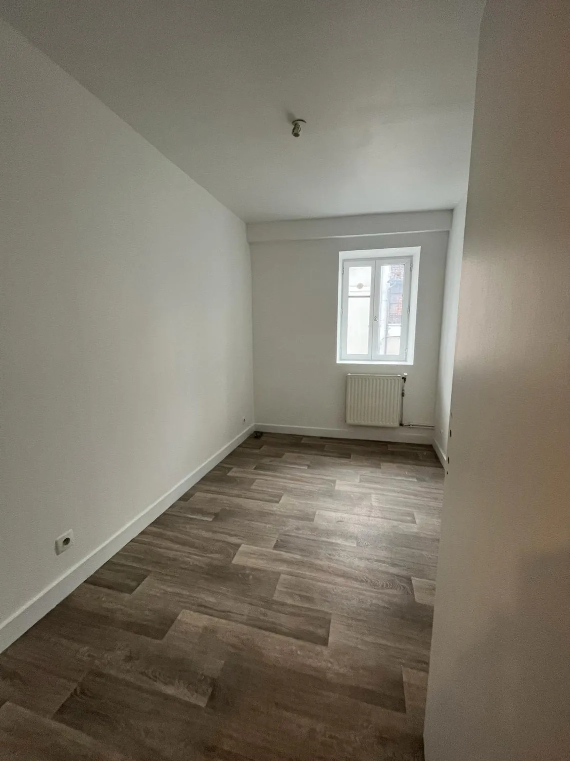 Pièce vide au sol carrelé imitation bois avec radiateur sous la fenêtre.