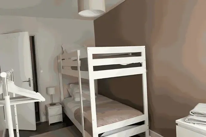 Chambre avec lits superposés en bois blanc et table de chevet.