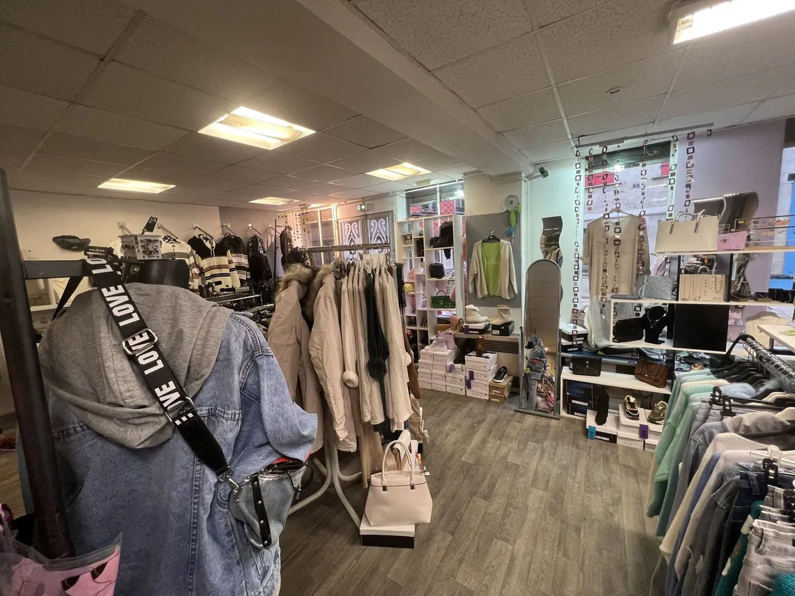 Fond de boutique avec portants de vêtements et rayonnages.